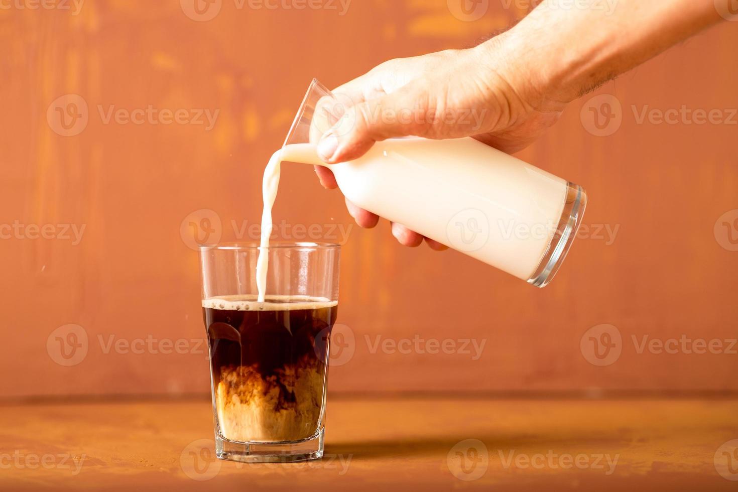 Hand is pouring milk to brewed coffee in studio with copy space. photo