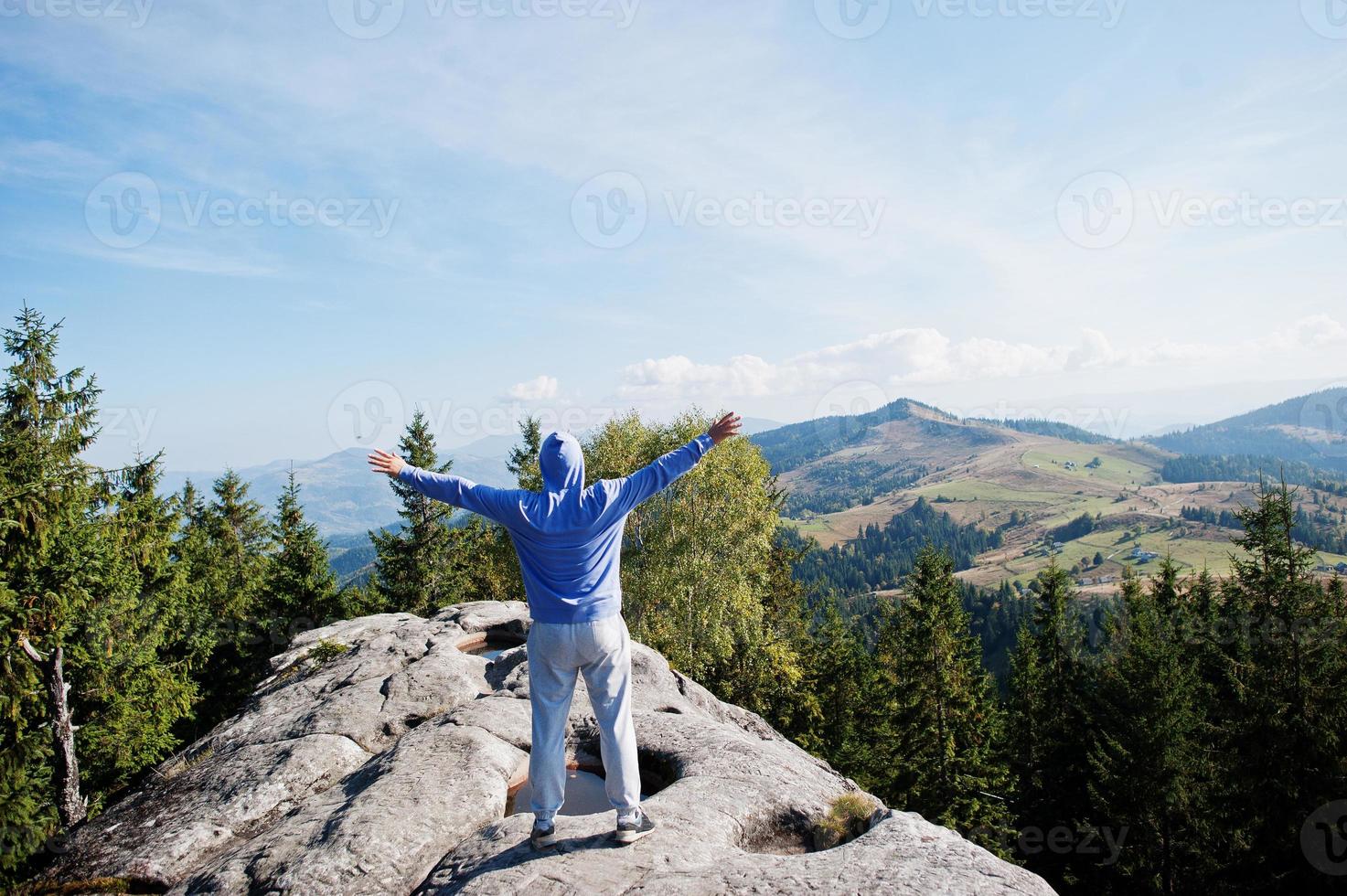 Happy hiker with hands in the air stand on rock. View over rocky valley. photo