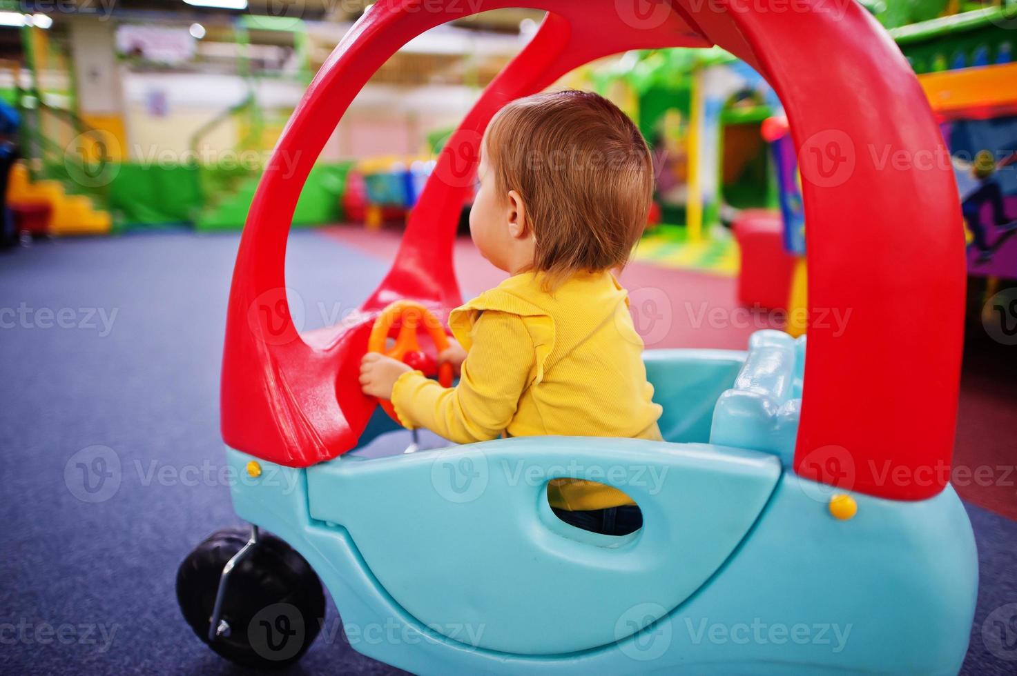 Cute baby girl rides on a plastic car in indoor play center. photo