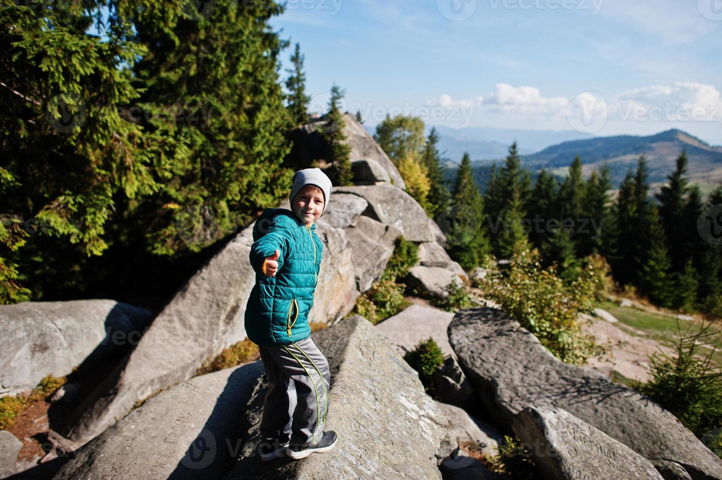 Children hiking on beautiful day in mountains, resting on rock and admire amazing view to mountain peaks. Active family vacation leisure with kids.Outdoor fun and healthy activity. photo