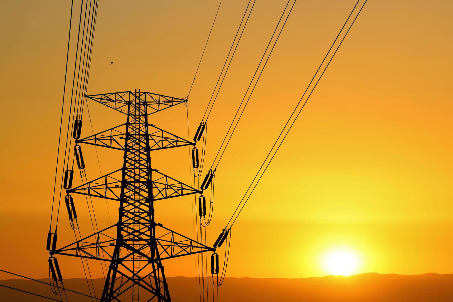 Silhouette of high voltage poles with electric wires. Silhouette of high voltage power line cables in an orange evening sunset. Steel structure of electric poles. electric power transmission concept photo