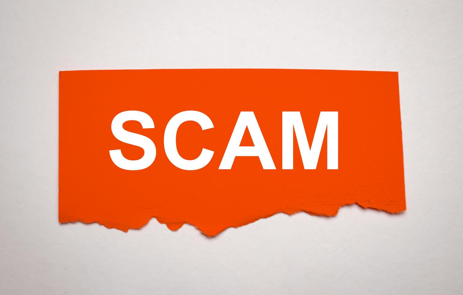 Red torn paper with a text of Scam on white cardboard photo
