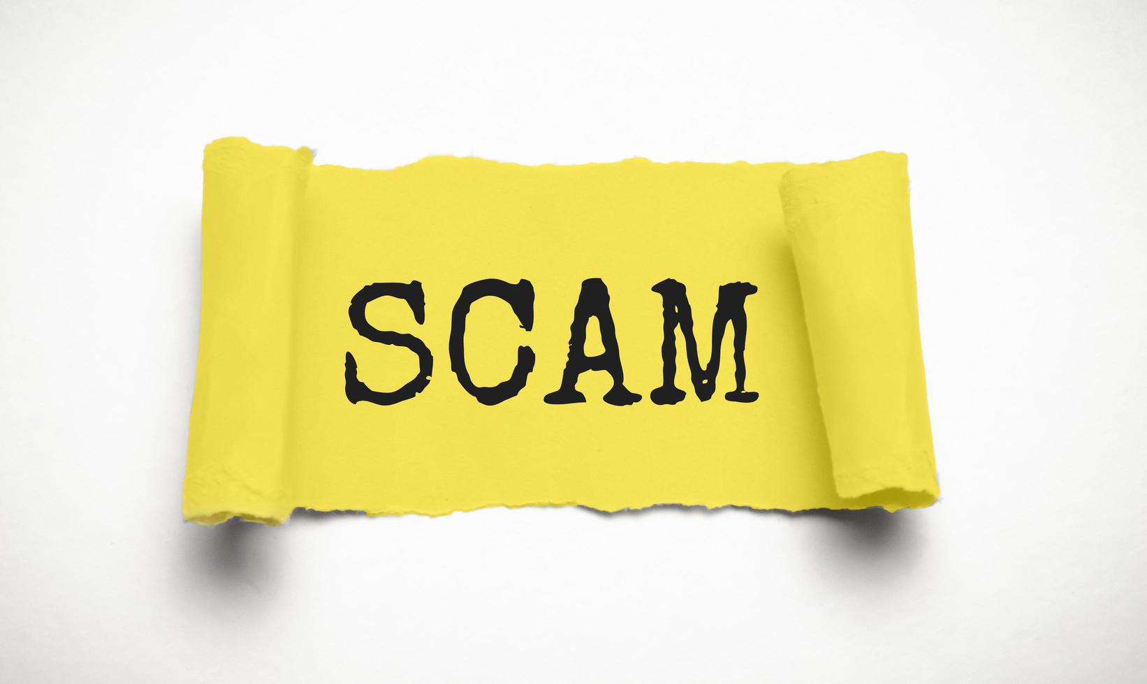 Yellow torn paper with a text of Scam on white cardboard photo
