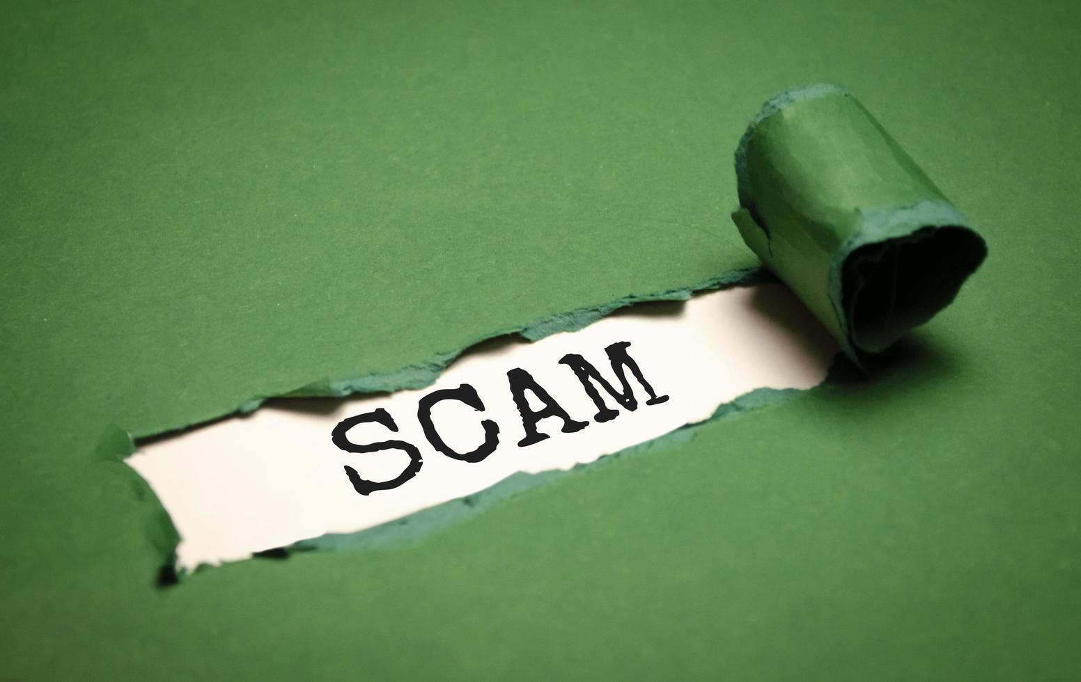 Green torn paper with a text of Scam on white cardboard photo