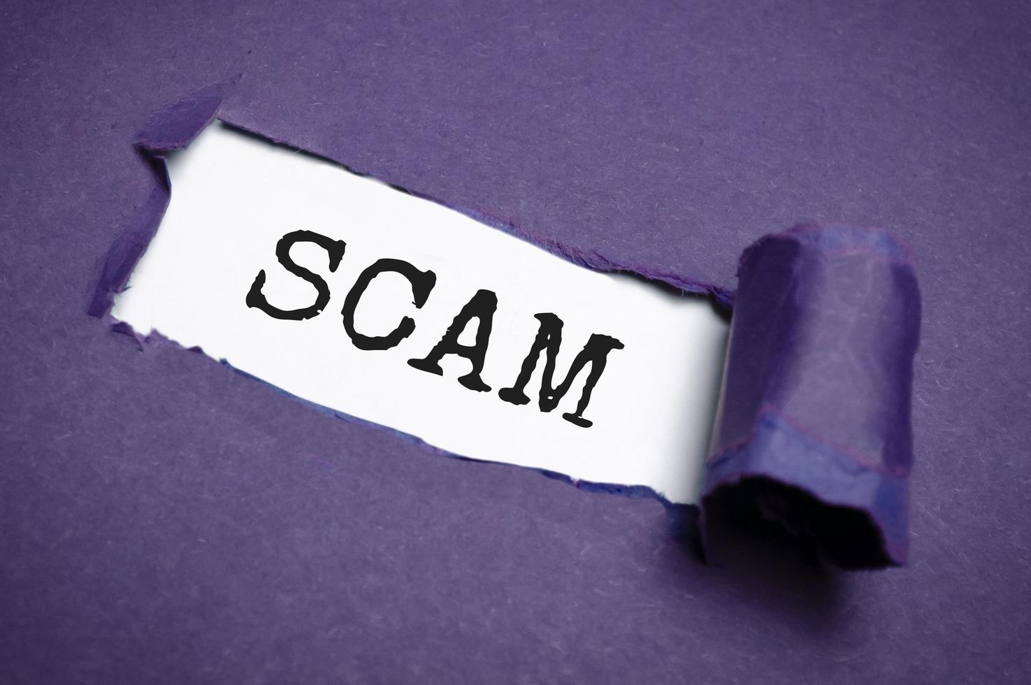 Purple torn paper with a text of Scam on white cardboard photo