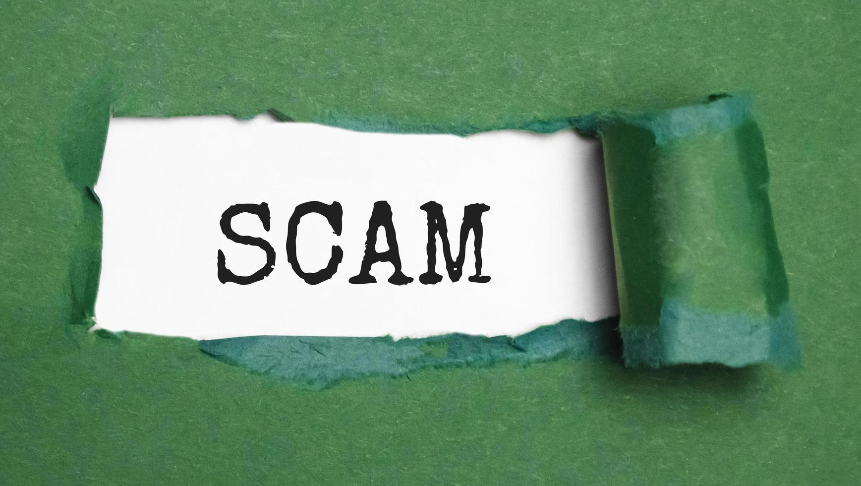Green torn paper with a text of Scam on white cardboard photo