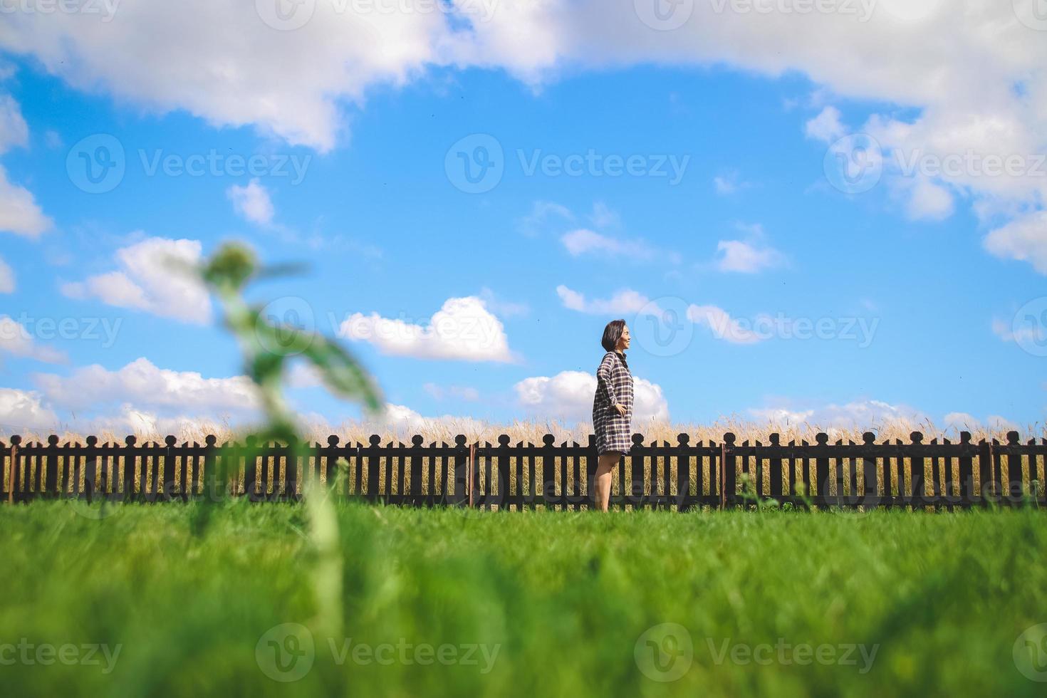 happy girl stand with wood fence in the green field under blue cloud sky. Beautiful landscape photo