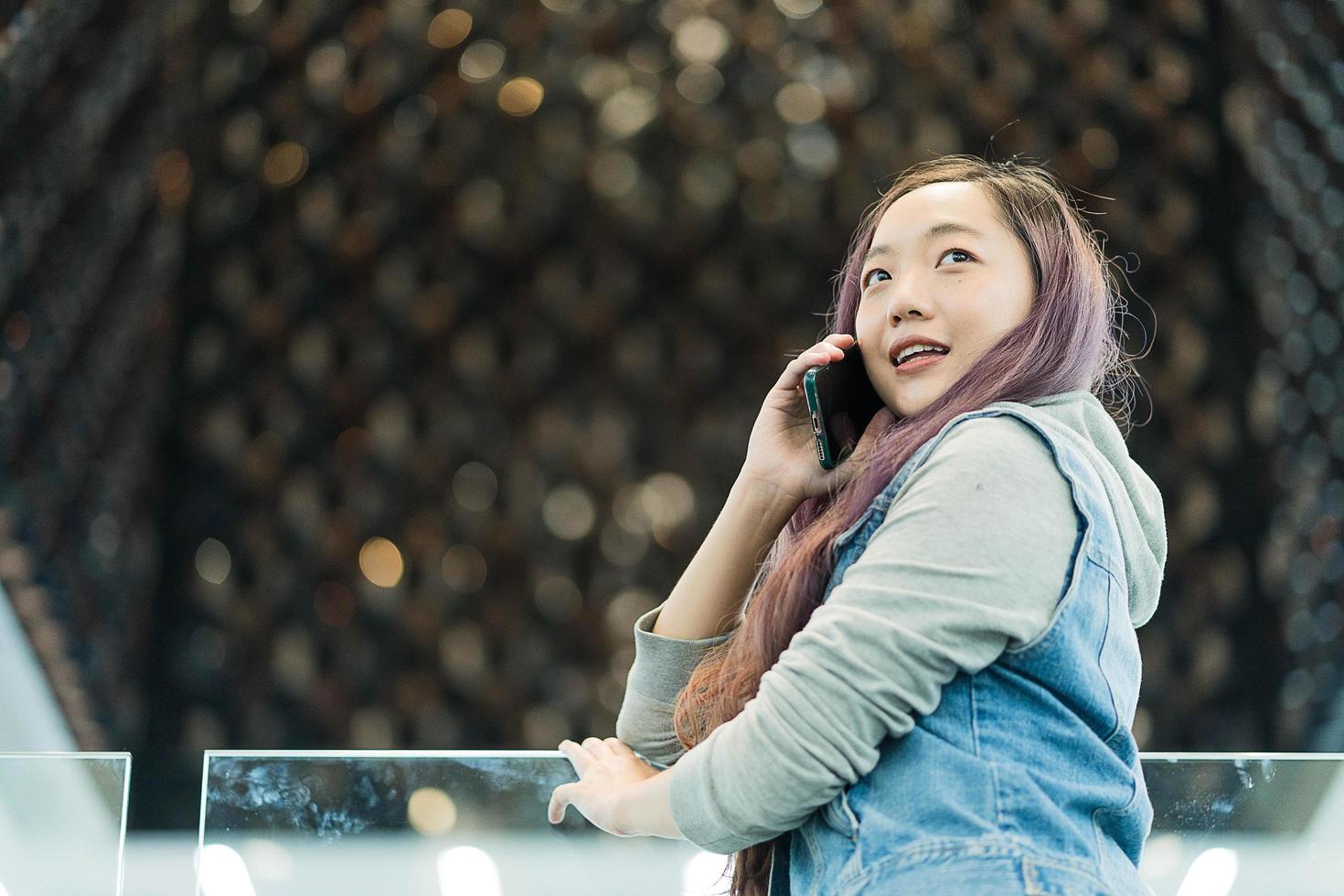 mujer joven alegre con ropa informal que tiene una conversación telefónica en un centro comercial, una mujer independiente sonriente que llama a un colega para compartir buenas noticias sobre negocios foto