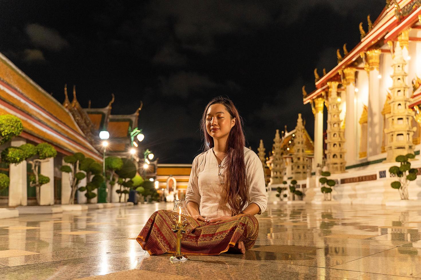 retrata a una mujer budista asiática con un vestido tradicional de tailandia sentada para meditar para rendir homenaje a la estatua de buda en wat suthat thepwararam en el día santo budista, el día de reposo budista, foto