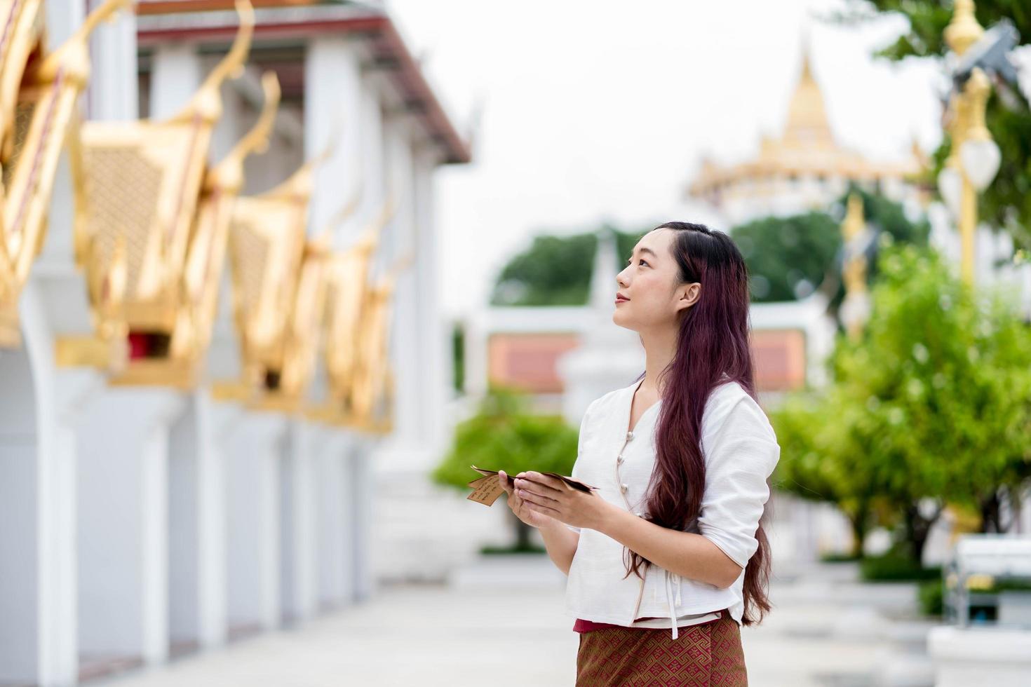 Asia woman wearing traditional dress of Thailand looking temple and hold Sanskrit ancient Tripitaka book of Lord Buddha dhamma, Sanctuary Ratchanatdaram bangkok. photo