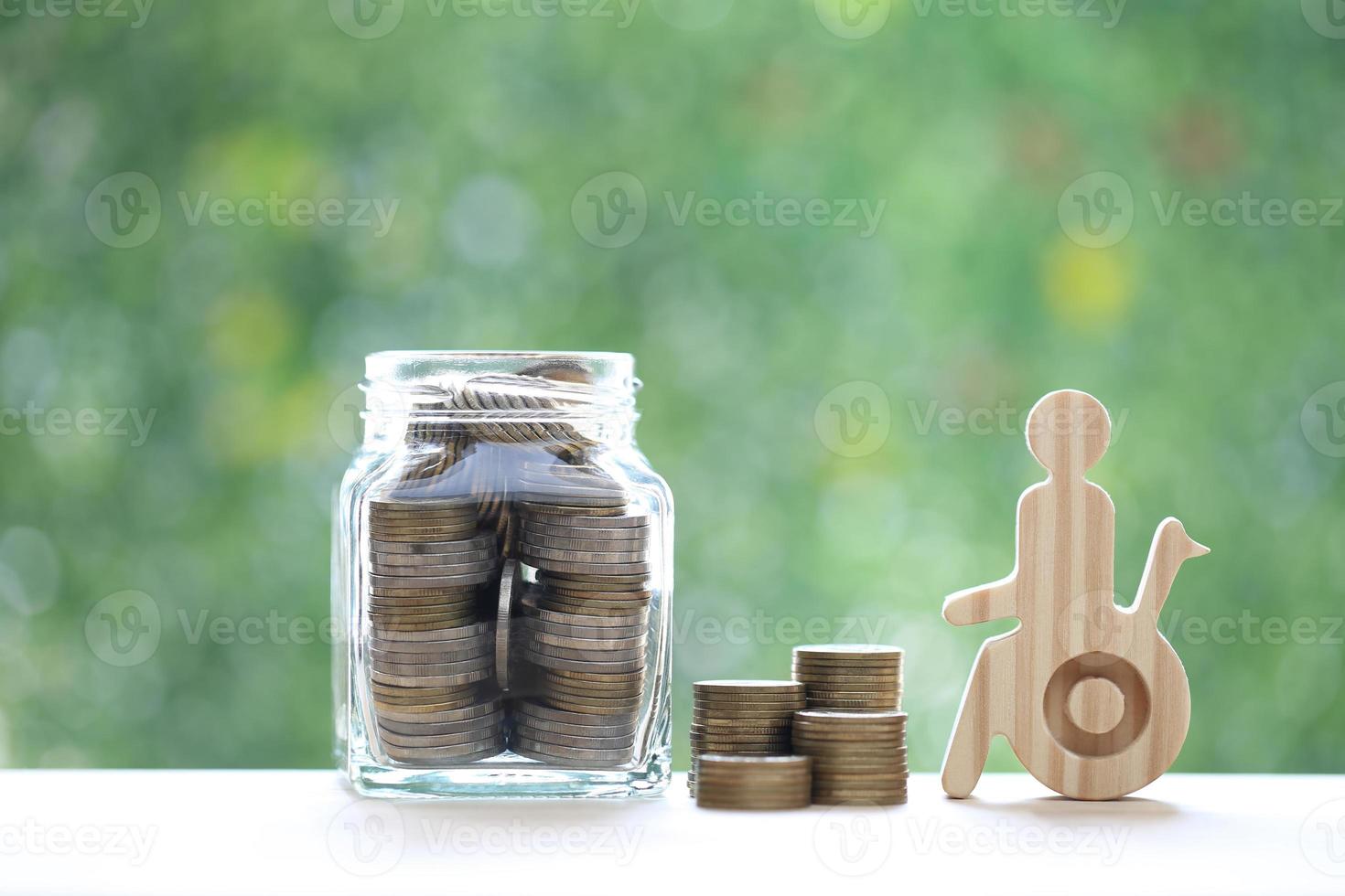 hombre en silla de ruedas y moneda de oro en la botella de vidrio sobre fondo verde natural, ahorre dinero para prepararse en el futuro y el concepto de persona discapacitada foto