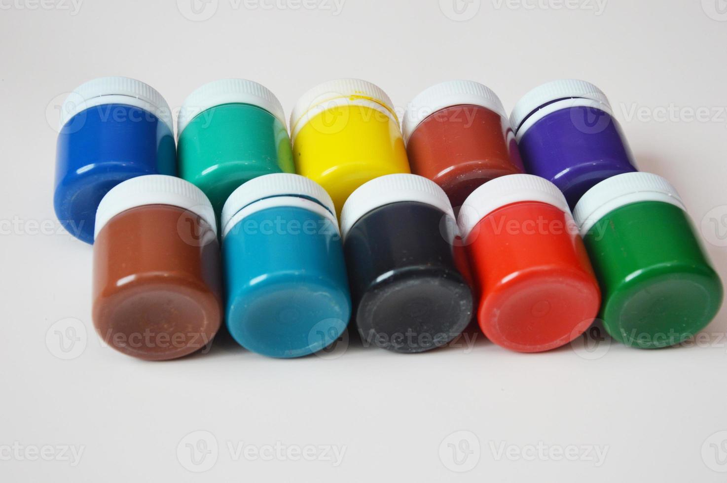 Closed jars of colored gouache, lying in a row on a light background. Multi-colored paints for creativity, drawing hobby. photo