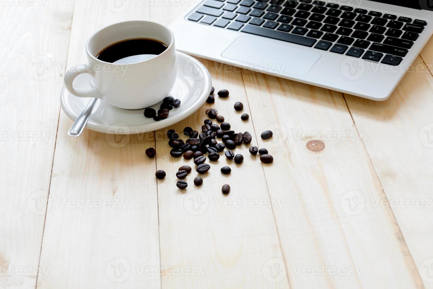 computadora portátil, taza de café recién hecho y granos de café foto