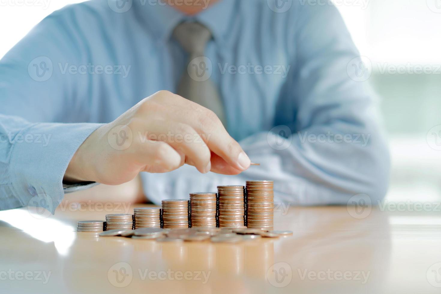 Businessman Sitting at Desk and Stacking Coins photo