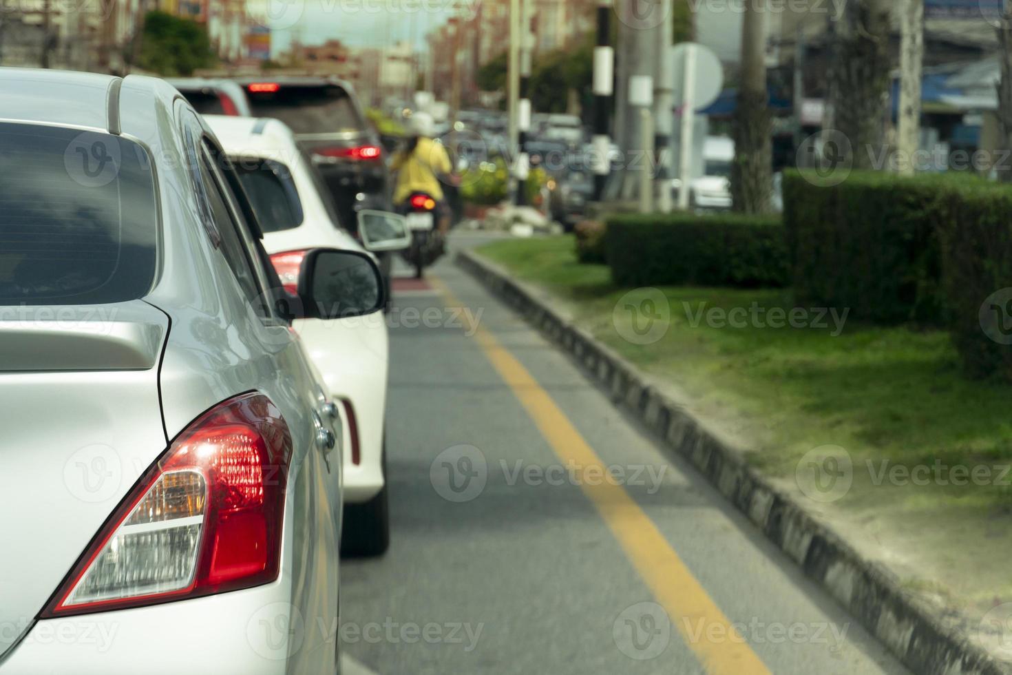 Rear side of silver car on the asphalt road heading towards the goal of the trip. Traveling for work during rush hour. Environment of blurred of other cars in the city. Island of green grass beside. photo
