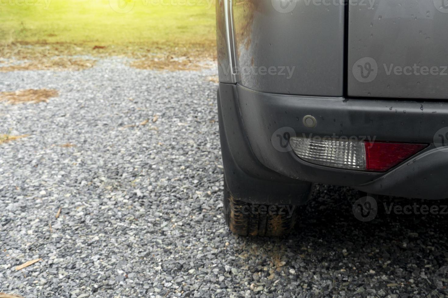 Down of rear side gray car parking on wide gravel floor. white blurred of green grass. environment of after rainy all area is wet from rain. photo