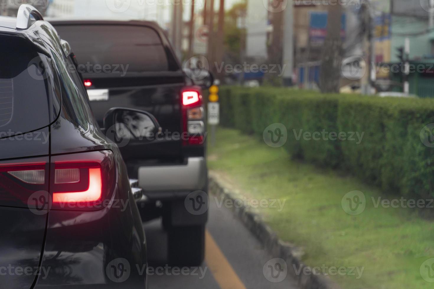 Rear side of black car on the asphalt road heading towards the goal of the trip. Traveling for work during rush hour. Environment of blurred of other cars in the city. Island of green grass beside. photo