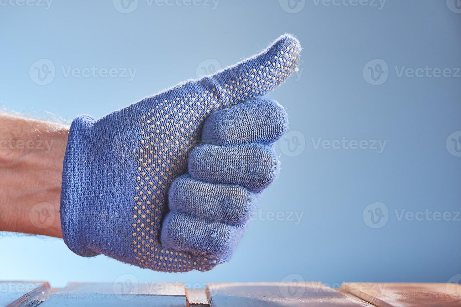 Hand wearing blue work glove with thumb up isolated on blue background. photo