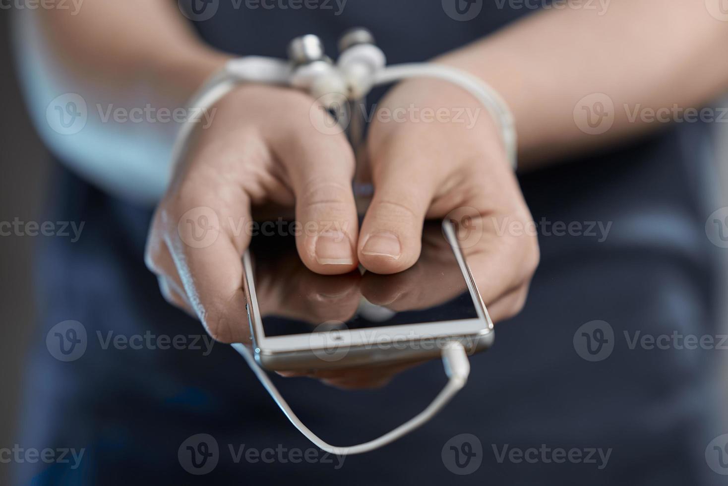 Hands of a young girl holding smartphone. Addiction to internet and social networks. Hands tied with wire. photo
