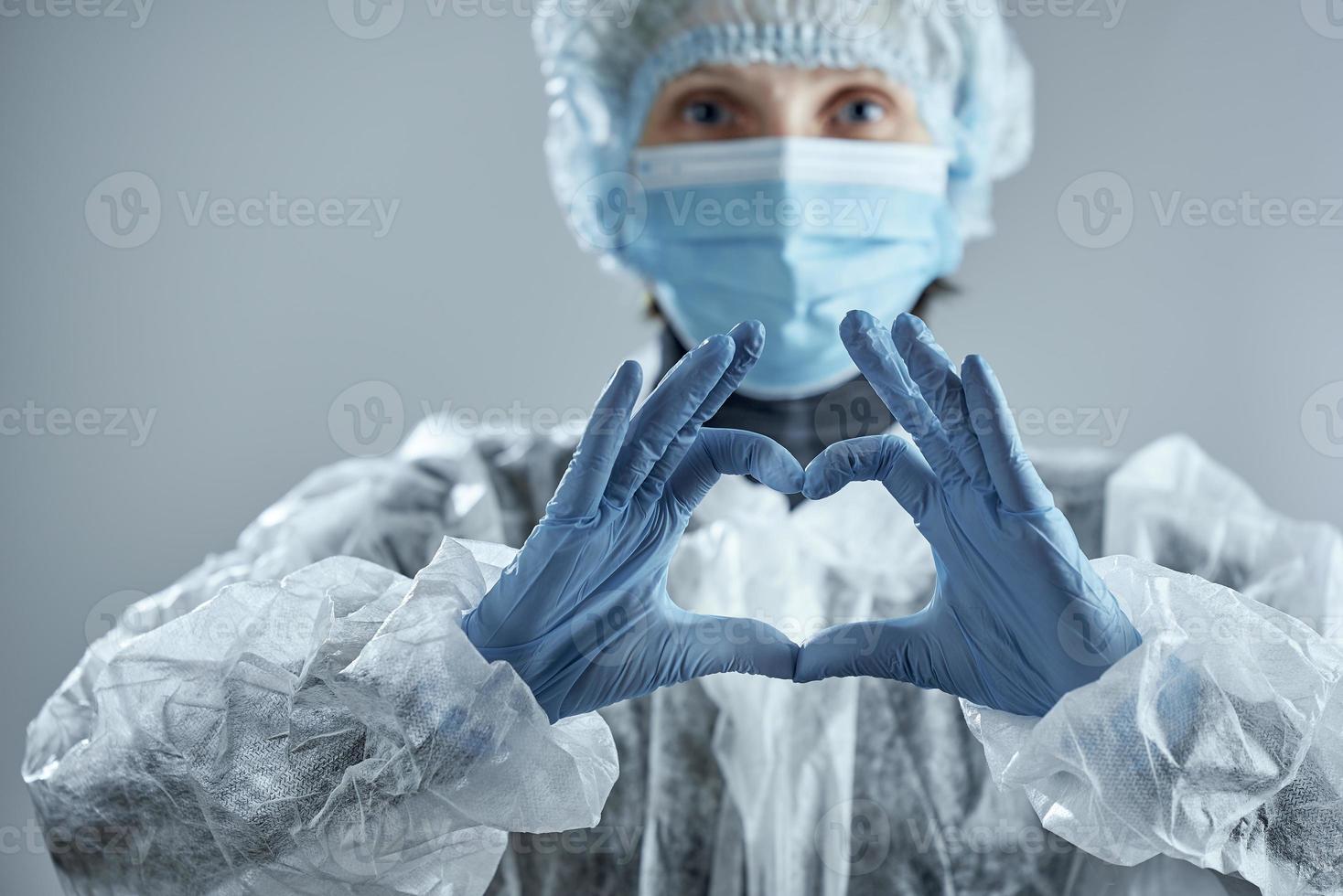 Medical worker in blur in medical mask, rubber gloves and suit makes a heart sign. Confronting coronavirus. photo