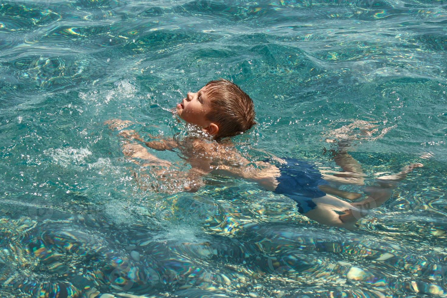 Child boy learning to swim in clear transparent sea. photo