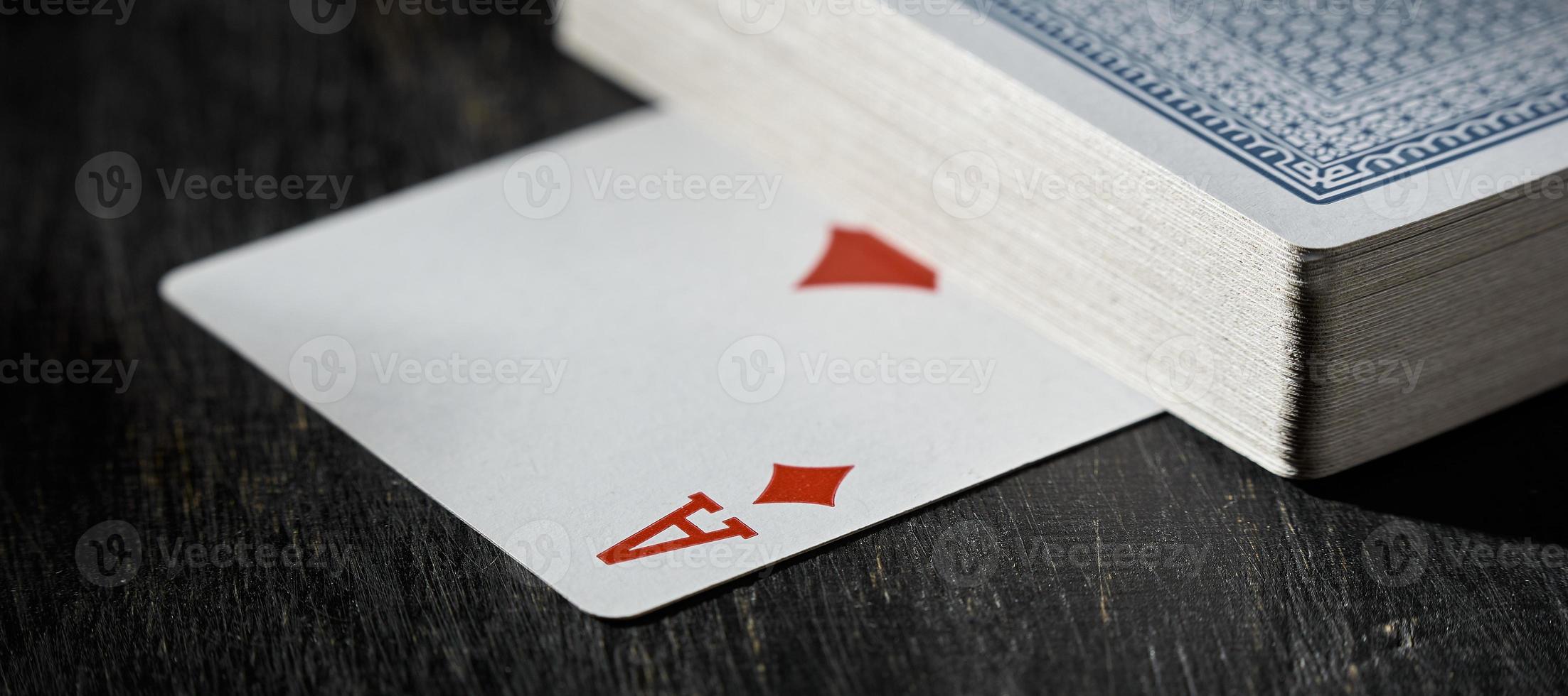 The ace of diamonds is under deck of cards on a wooden table. photo