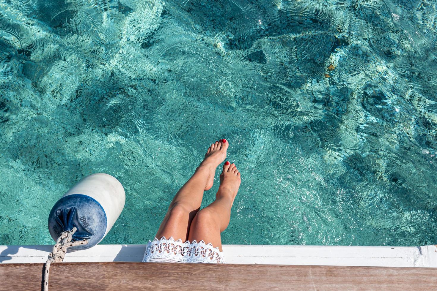 women's legs hanging from the yacht with clear blue water under photo