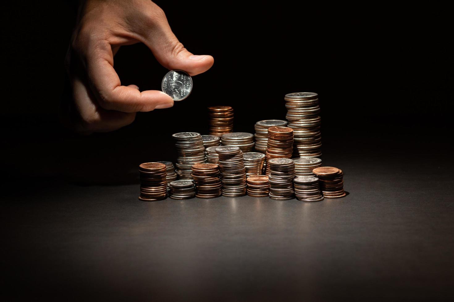 un montón de monedas en una mesa y la mano agregando monedas al montón foto