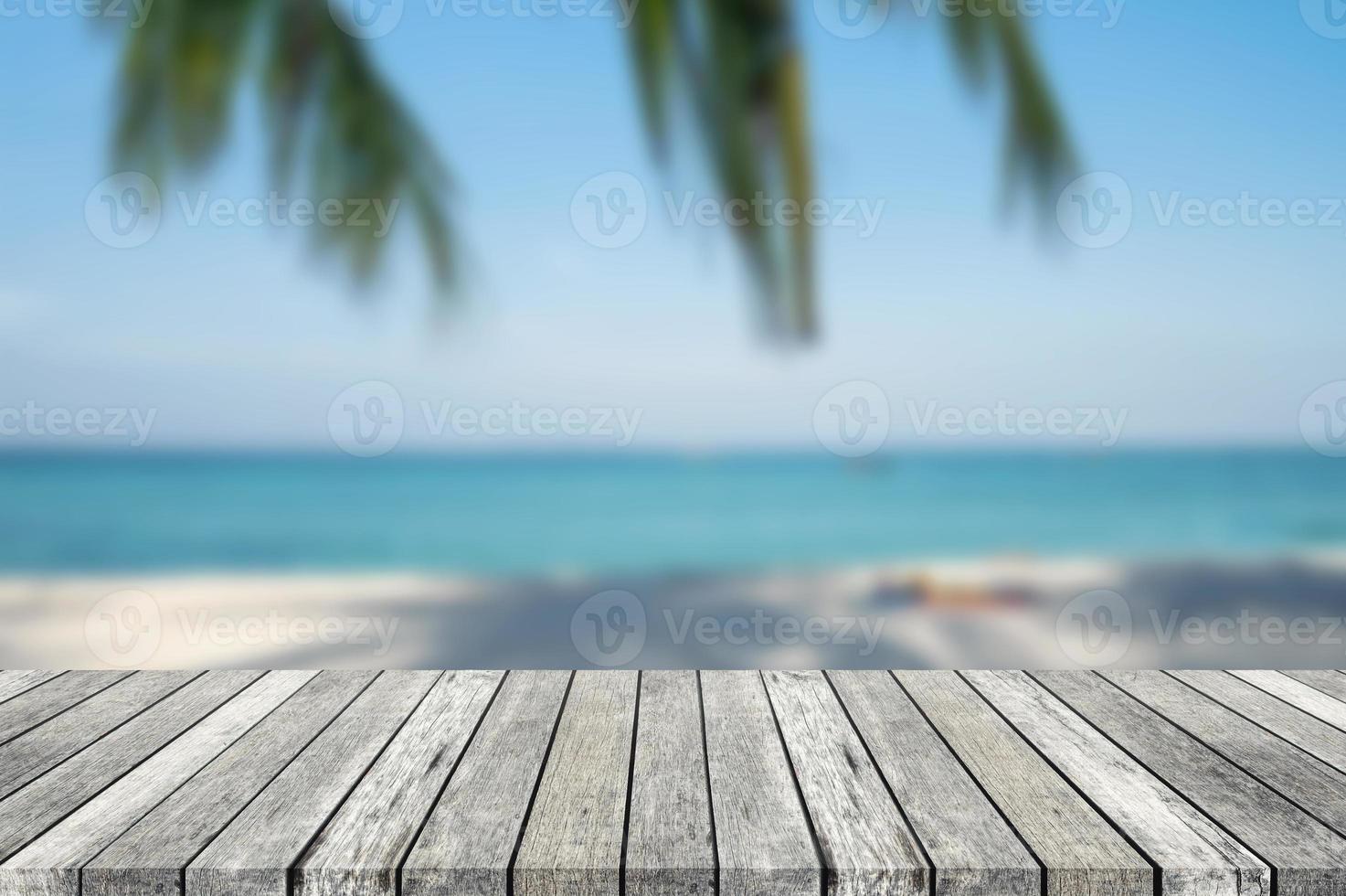 Wooden gray tabletop with blurred scene of tropical beach and plam leaf photo