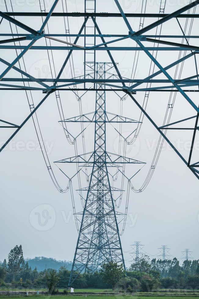 fila de poste de alto voltaje, gran torre eléctrica de transmisión con cable en campo de arroz con cielo azul en el campo foto