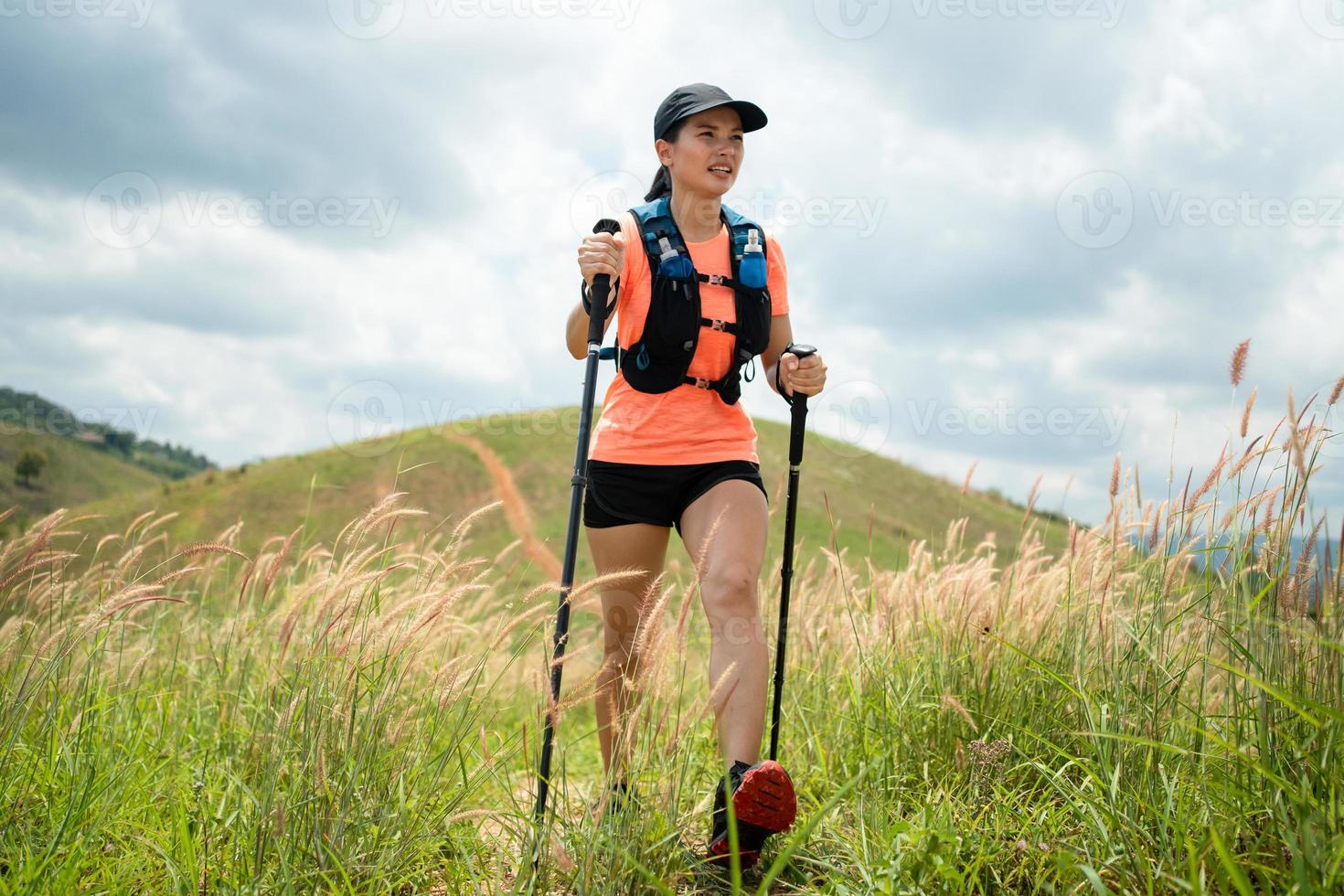 sendero activo para mujeres jóvenes que atraviesa un prado en un sendero cubierto de hierba en lo alto de las montañas por la tarde con bastón de trekking foto