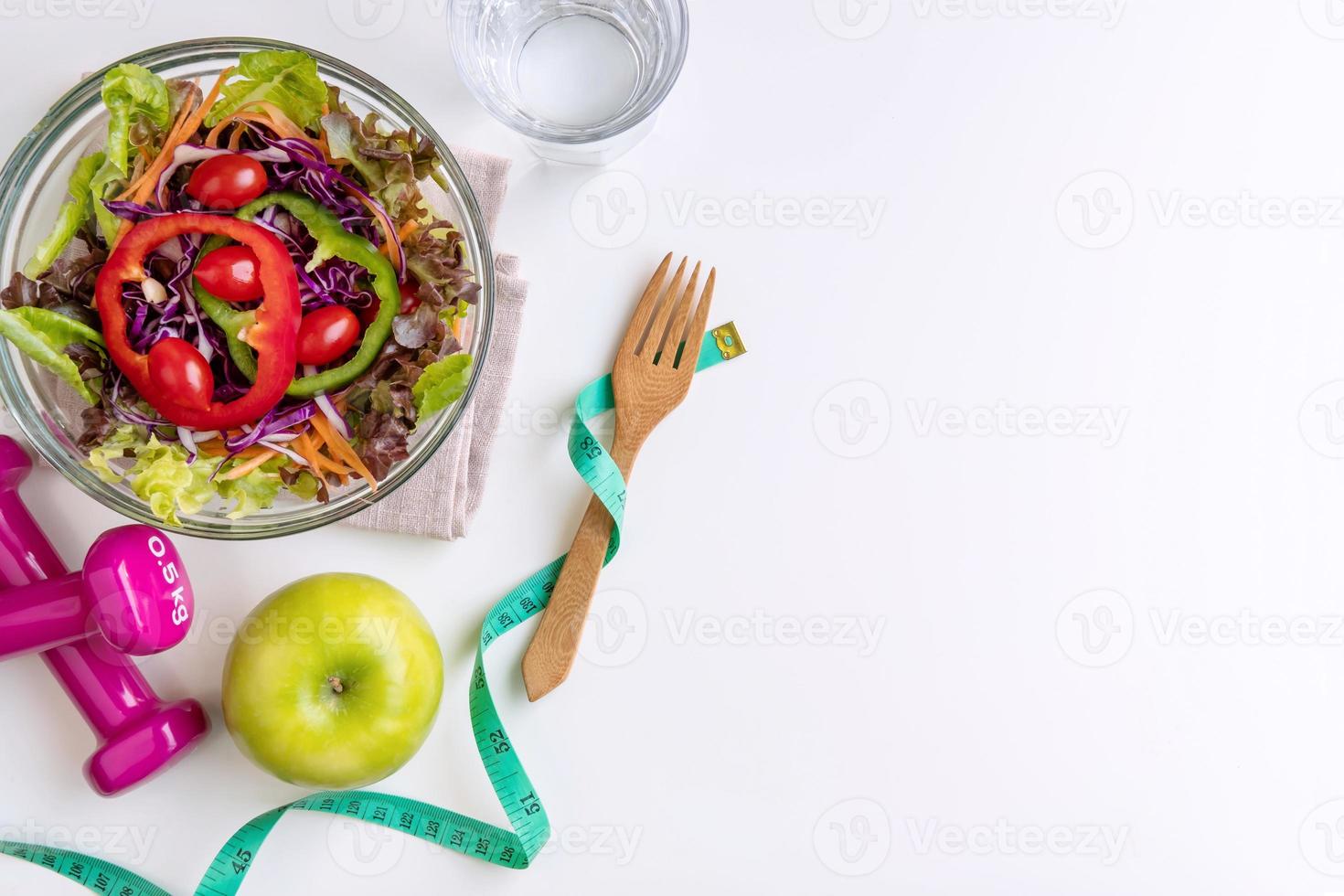 Fresh salad with green apple, dumbbell and measuring tape on white background. Diet, healthy eating concept photo