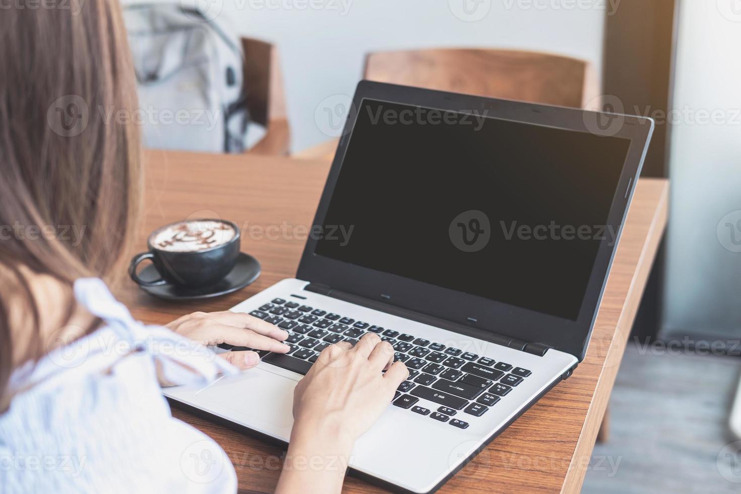 mujer joven que usa un teléfono inteligente y una computadora portátil con una taza de café en la cafetería foto