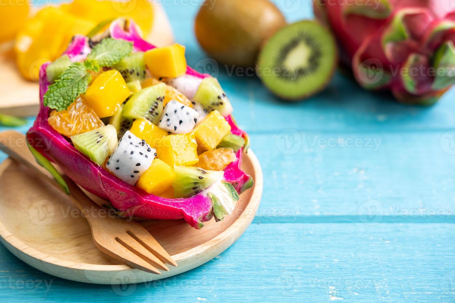 mezclar ensalada de frutas tropicales servida en media fruta de dragón en una mesa de madera foto