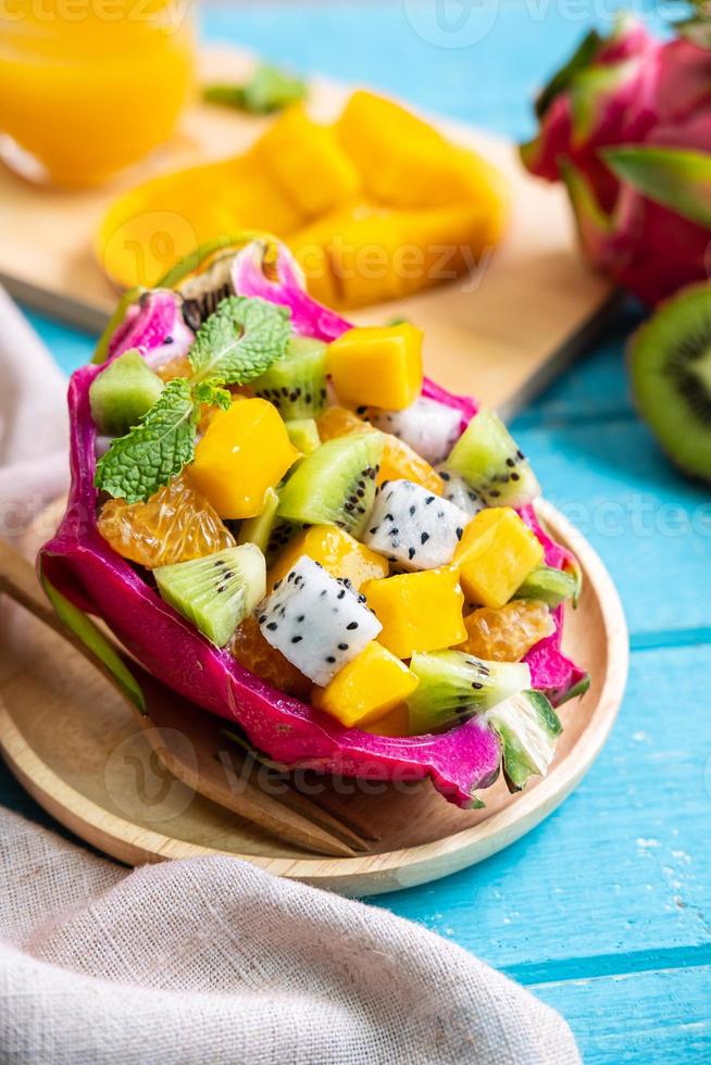 mezclar ensalada de frutas tropicales servida en media fruta de dragón en una mesa de madera foto