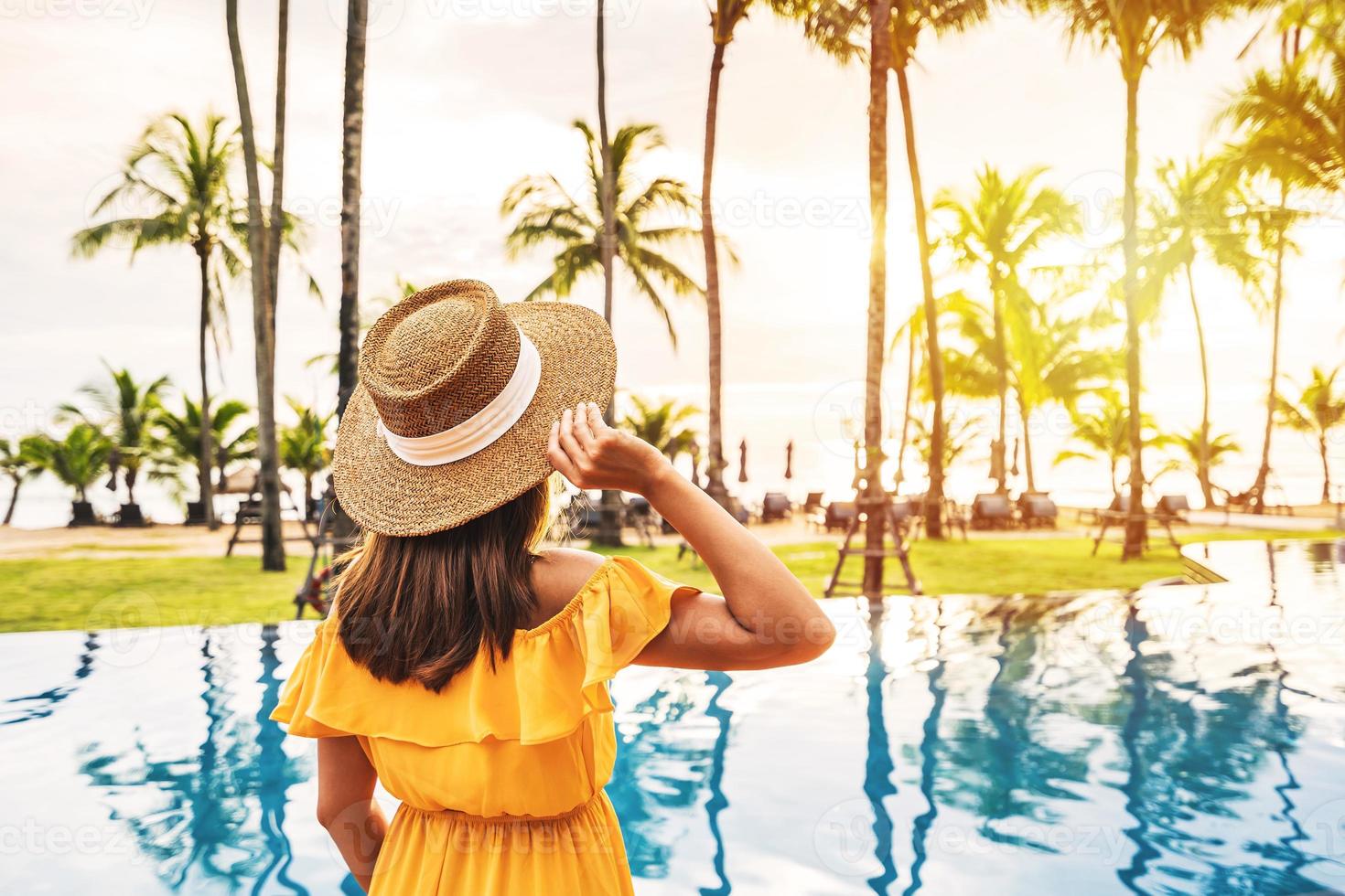 Young woman traveler relaxing and enjoying the sunset by a tropical resort pool while traveling for summer vacation photo
