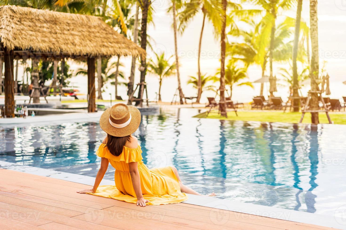 Young woman traveler relaxing and enjoying the sunset by a tropical resort pool while traveling for summer vacation photo