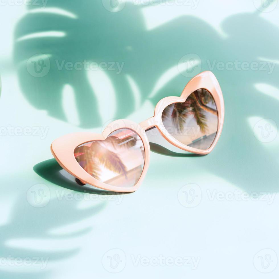 Sunglasses with a view of the beach reflecting in front of the lens against a backdrop of shadow of tropical leaves photo