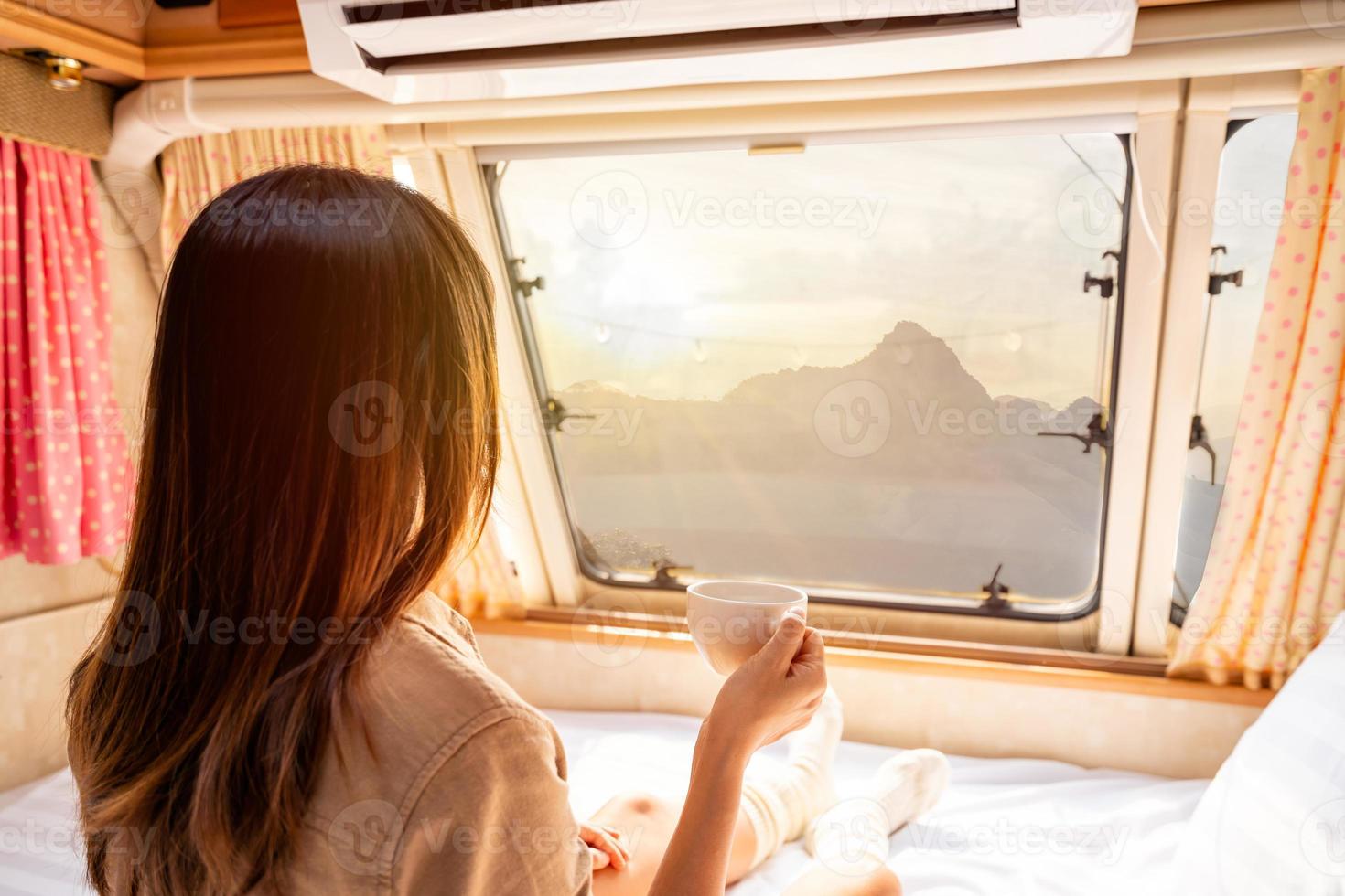 Young woman traveler with cup of coffee laying in camper van and looking beautiful landscape while road trip traveling on vacation photo