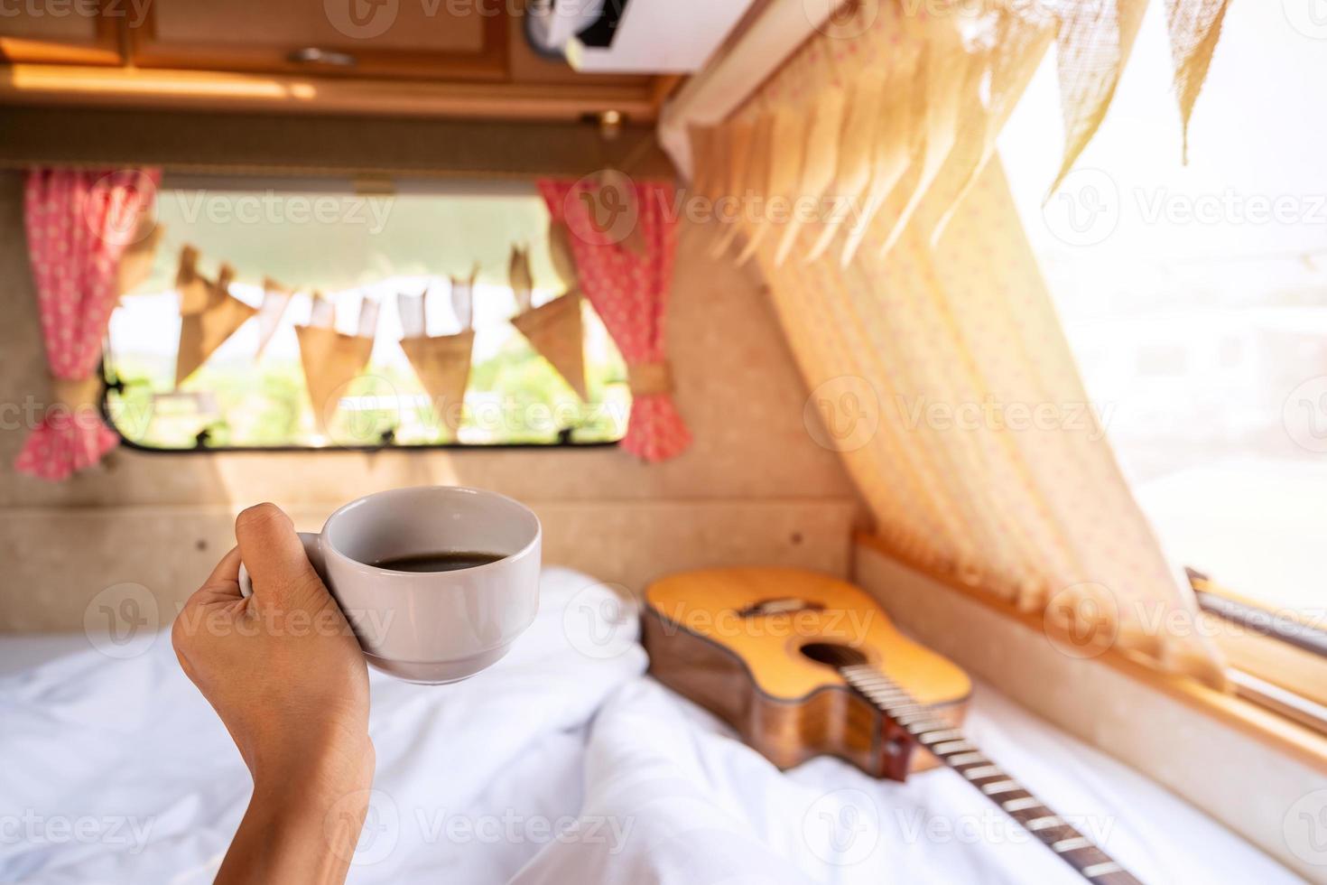 joven viajera con una taza de café recostada en una autocaravana y mirando un hermoso paisaje mientras viaja por carretera de vacaciones foto