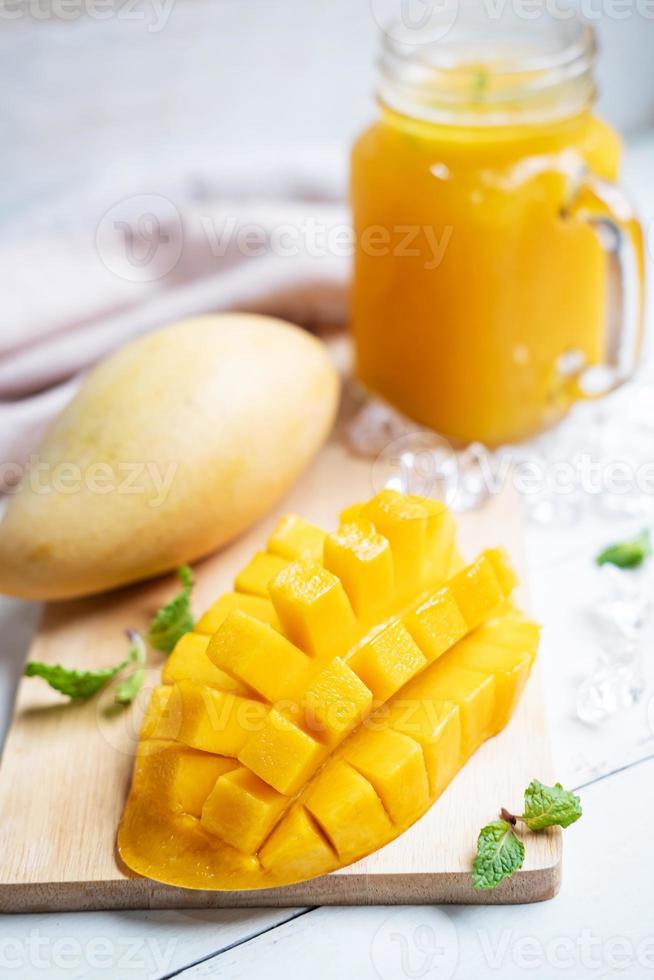 refrescantes batidos de mango en vidrio con mango maduro sobre mesa de madera blanca foto