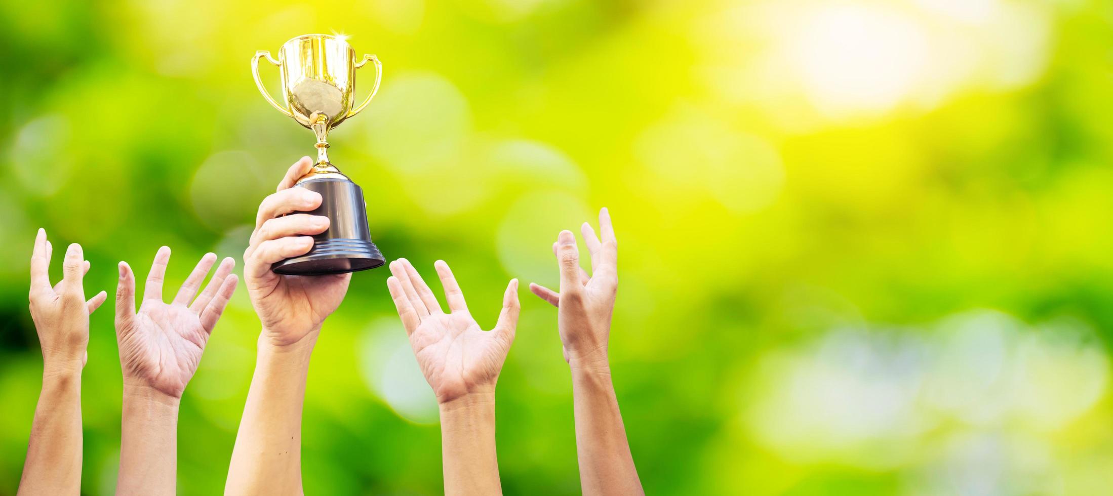 Many hands raised up. Winner is holding trophy cup in hand. on blurred green background photo