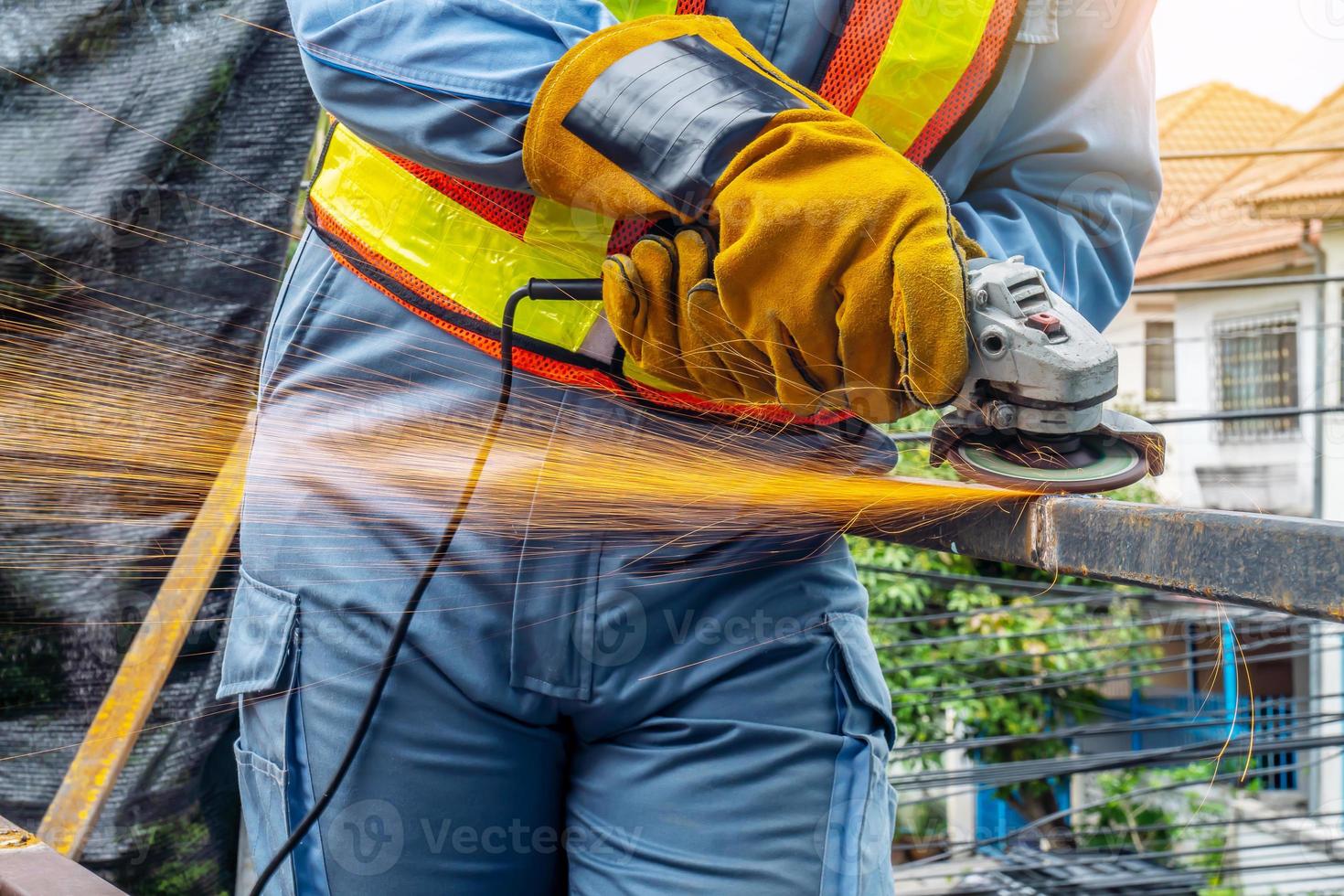 Young man welder in a working blue overall and working gloves grinds a metal object with a angle grinder in the garage, bright sparks fly to the sides photo