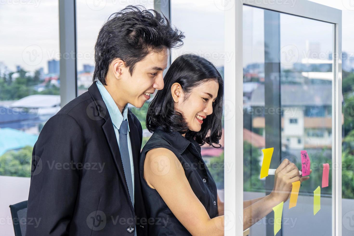 Asian creative business women and man are writing note on the text sheet after thinking new idea and planning project with colleague ,Group of employee brainstorming idea on glass wall and sticky photo