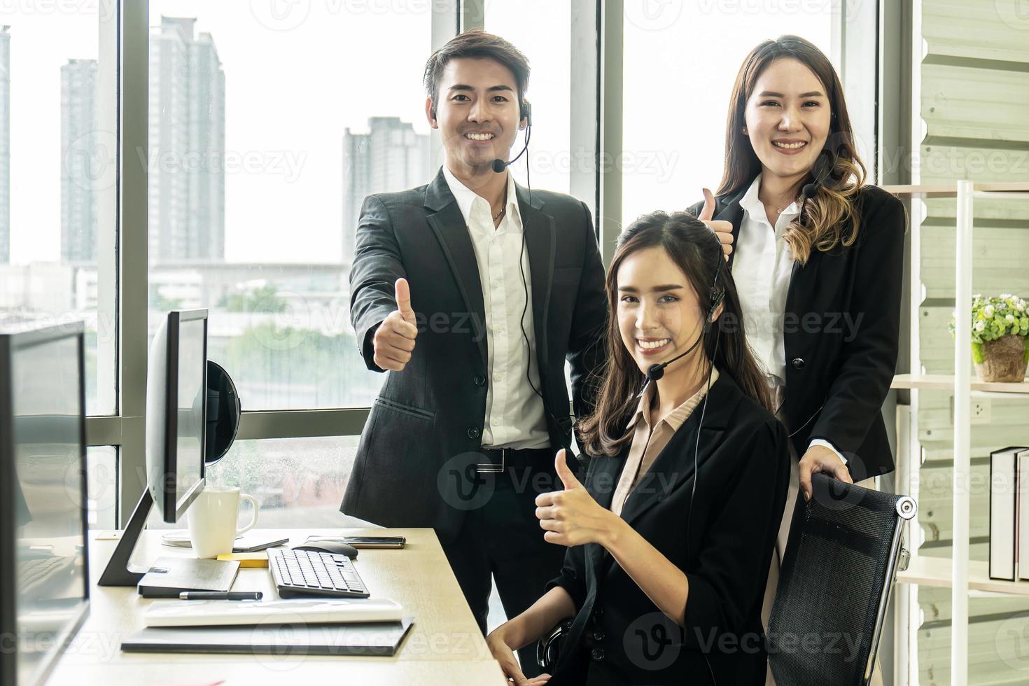 Handsome and Beautiful of call center or customer support operator smiling and showing thumbs up in headphones in office. Service mind concept photo
