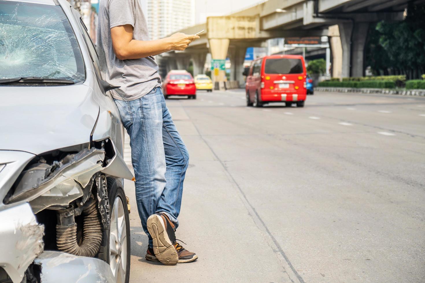 Man using smartphone help calling Insurance company or recovery service at roadside after traffic accident photo