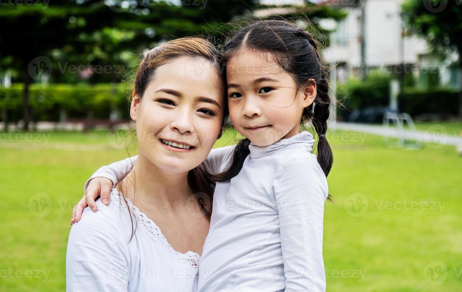 Cute asian mother and daughter smiling and hugging in love playing in the park photo