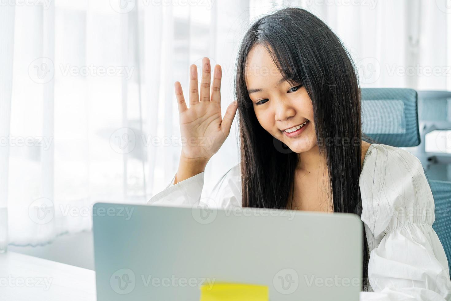 Smiling asian young female in headphones wave hand to laptop screen greet teacher tutor at lesson consultation. Happy young woman say hi hello to friend speaking from university by video call photo