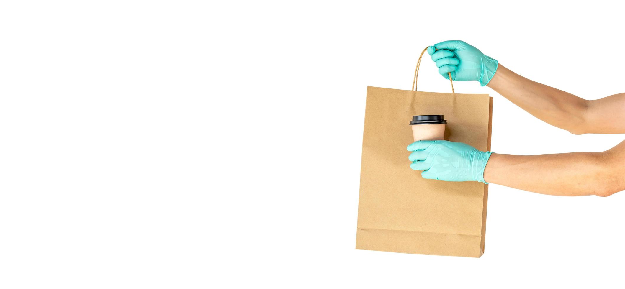 Delivery man hand in sterile gloves holding food in craft paper bag  and coffee isolated on white background with copy space, safe delivery during a virus quarantine pandemic, stay home. photo