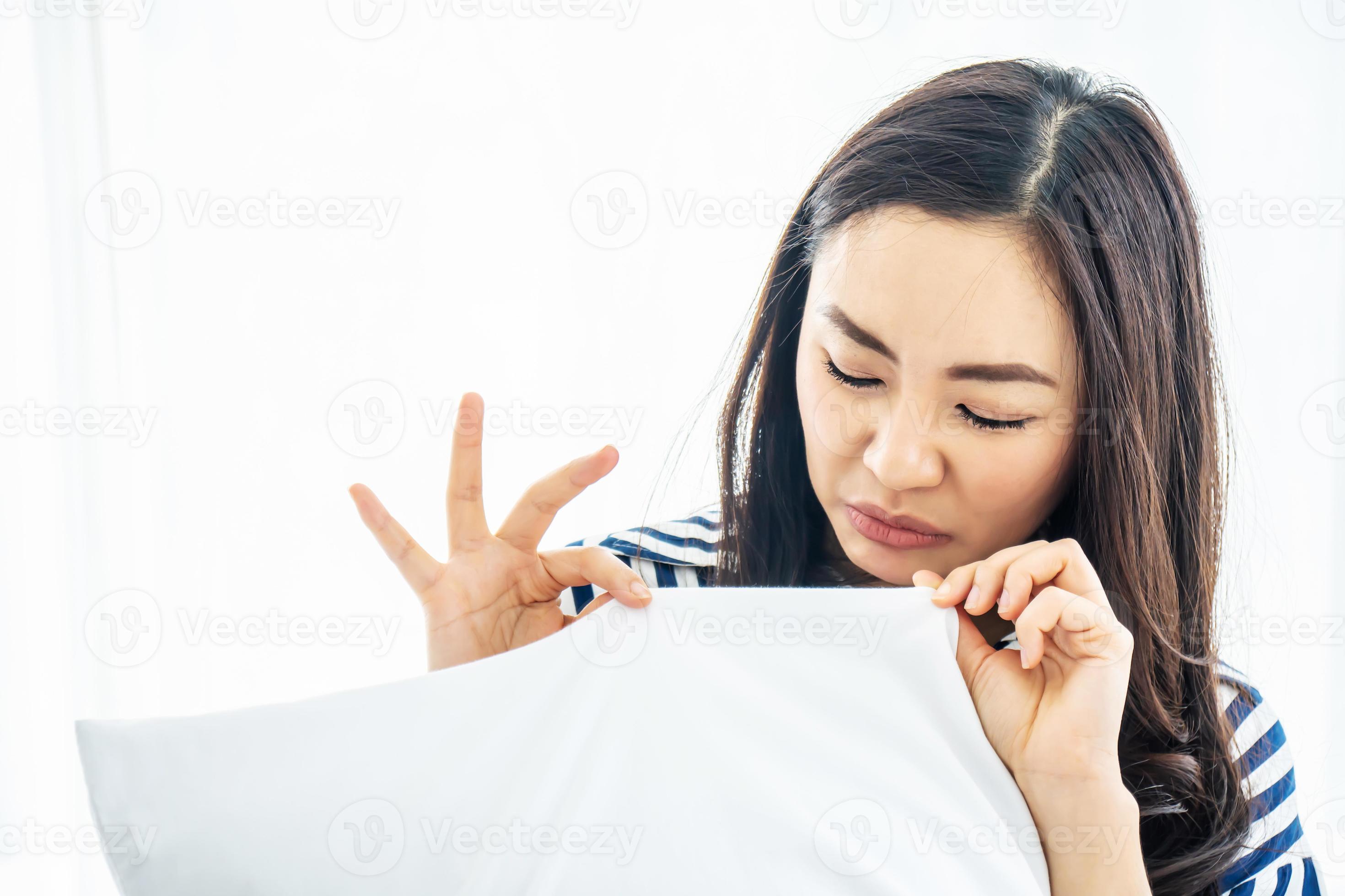 Beautiful woman sniffing a white pillow with a foul odor or musty smell